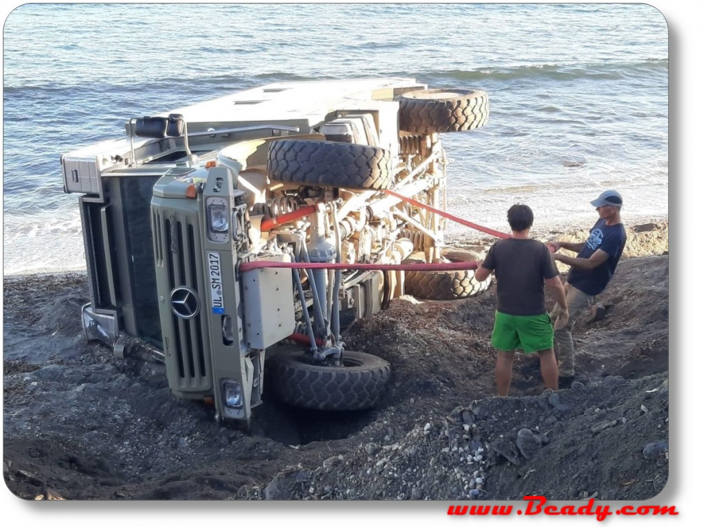 Unimog overlander camper fallen over, on it's side, by sea on beach crash with straps to recover