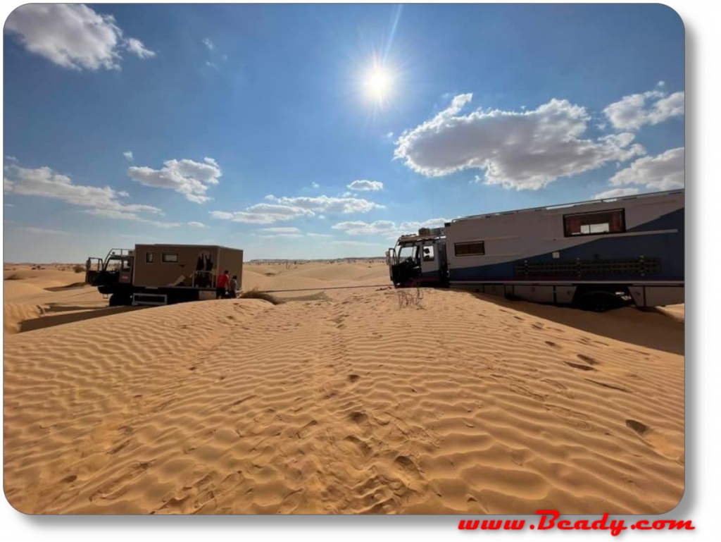 Kamaz overland truck stuck in the dunes being towed by another truck
